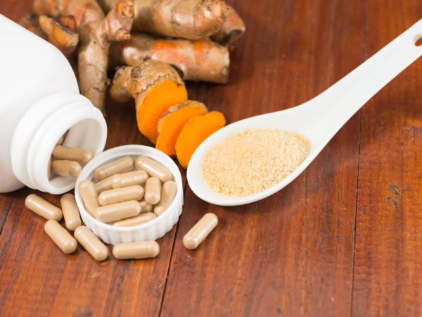 Turmeric herbal capsules in white bottle ,fresh turmeric root and turmeric powder in ceramic spoon on wooden background