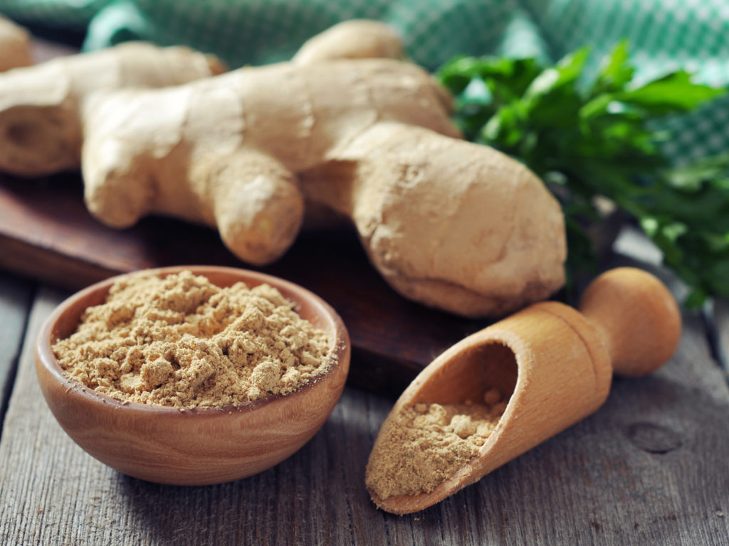 Fresh ginger root and ground ginger spice on wooden background