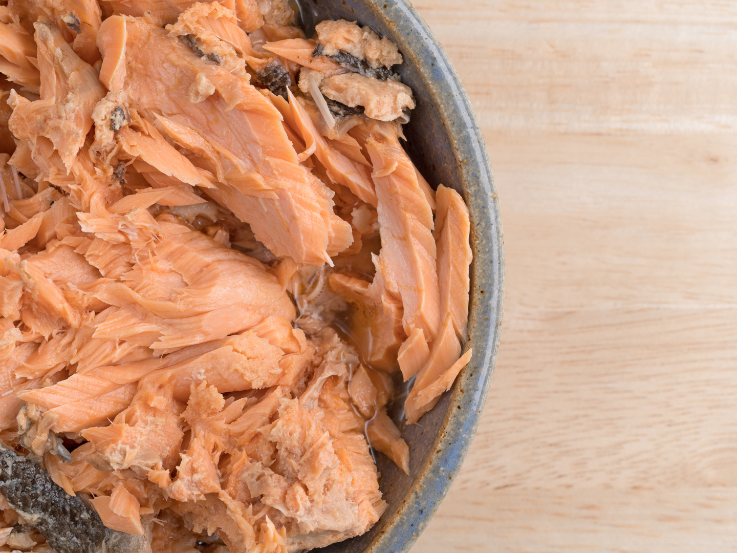 Top close view of Pacific canned pink salmon in an old stoneware bowl atop a wood table.