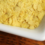 Small dish of nutritional yeast on a wooden background.  Shot in studio with a Canon 5D Mark III.