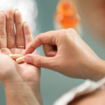 Close up view of young woman holding ginseng vitamins and minerals pills in hand with capsule bottle on table. High angle view