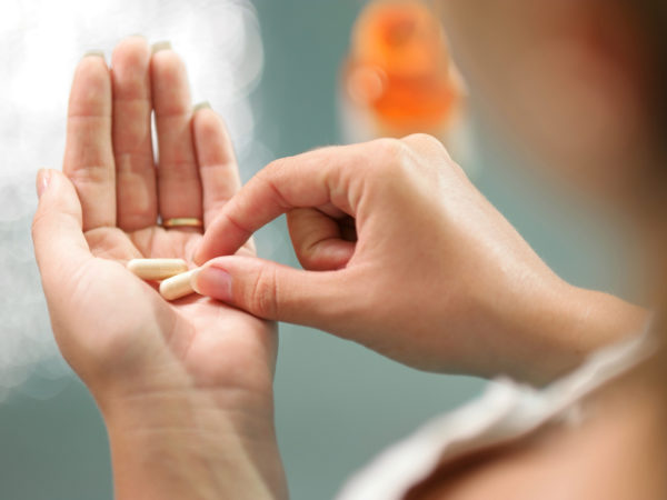 Close up view of young woman holding ginseng vitamins and minerals pills in hand with capsule bottle on table. High angle view