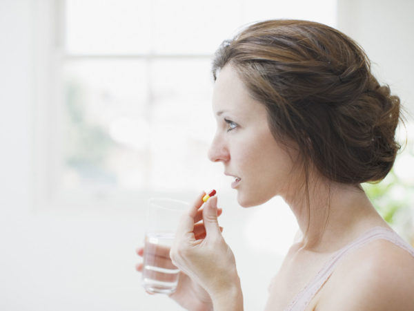 Woman holding glass of water and taking capsule