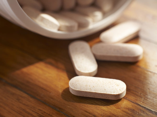 Close up of four large tablets spilling out of container onto wood surface. Very shallow DOF. Focus on front tablet.