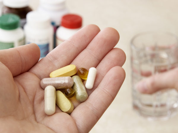 Health conscious person holding a variety of natural vitamins, supplements and herbal remedies, while their other hand holds a glass of water ready to take the pills.