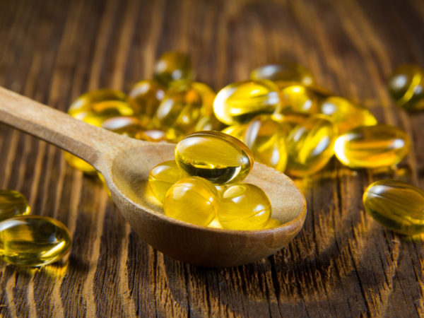 Cod-liver oil, omega3, vitamin D capsules on wooden spoon