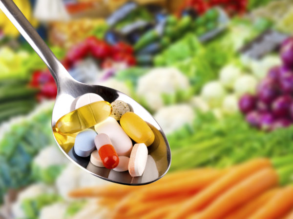 spoon with variety of pills, dietary supplements on blurred vegetables background