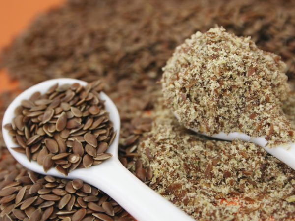 Whole and ground flaxseed (linseed) against an orange background.