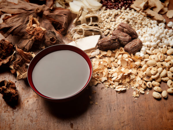 Subject: A variety of Chinese herbal medicine ingredients and the resulting tonic tea displayed on wooden table.