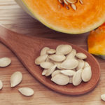 Pumkin seeds inside of wooden spoon near the pumpkin. Close up. Diet concept.