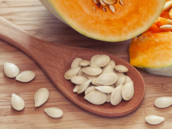 Pumkin seeds inside of wooden spoon near the pumpkin. Close up. Diet concept.