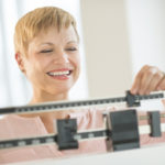Happy mature woman adjusting balance weight scale at health club