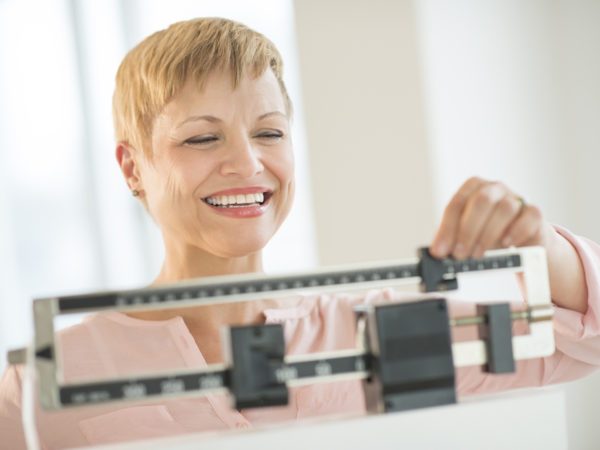 Happy mature woman adjusting balance weight scale at health club