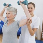 Female trainer assisting senior woman lifting weights in gym