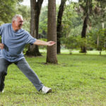 Senior man (60s) exercising in park, practicing tai chi.