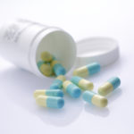 green-and-yellow capsules spilling from a prescription medicine bottle across the corner of a prescription ; shot with very shallow depth of field ,