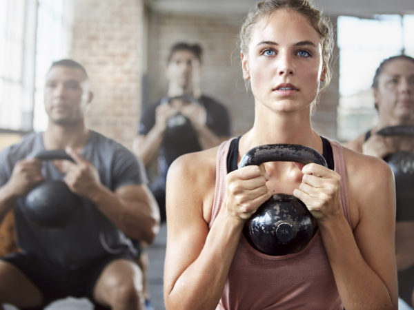 Shot of a group of people doing squats with a kettle bell in a gym