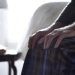 Cropped image of senior man sitting on bed with his hands on knees