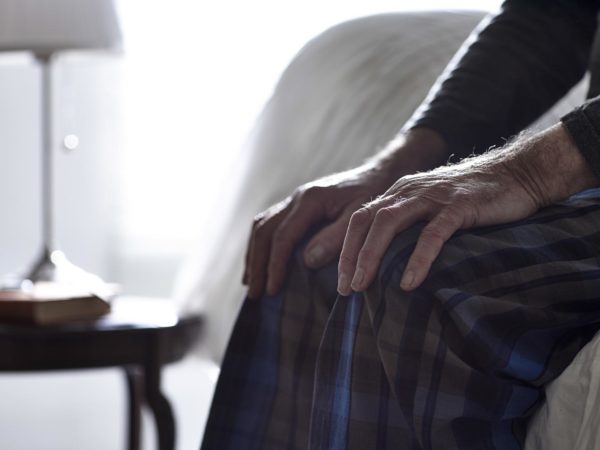 Cropped image of senior man sitting on bed with his hands on knees