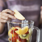 A closeup cropped shot of a woman&#039;s hand putting sliced fruits into a blender