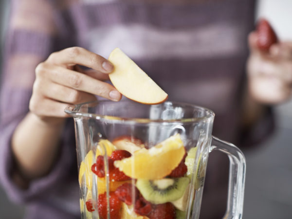 A closeup cropped shot of a woman&#039;s hand putting sliced fruits into a blender