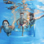 Happy family - father and mother with baby boy swimming and diving underwater with fun in blue pool. Healthy lifestyle, active parents, and people water sports activity on summer vacation with child