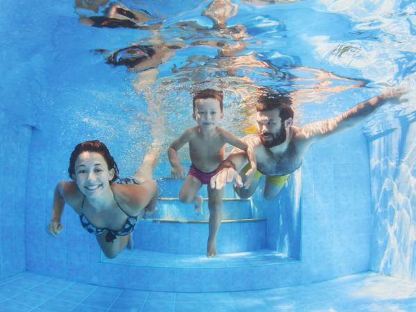 Happy family - father and mother with baby boy swimming and diving underwater with fun in blue pool. Healthy lifestyle, active parents, and people water sports activity on summer vacation with child