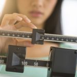 Midsection of mid adult Asian woman adjusting balance weight scale