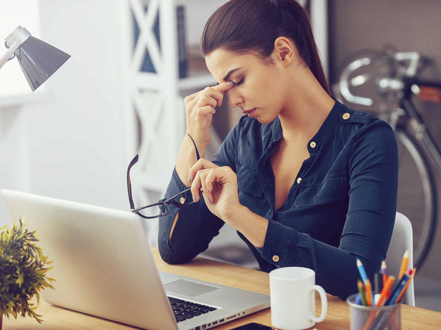 Frustrated young woman keeping eyes closed and massaging nose while sitting at her working place in office