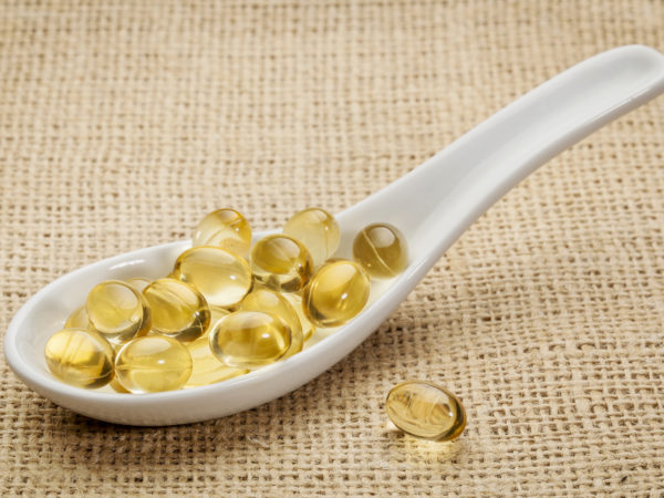 Vitamin E oil capsules on a ceramic spoon against canvas background.