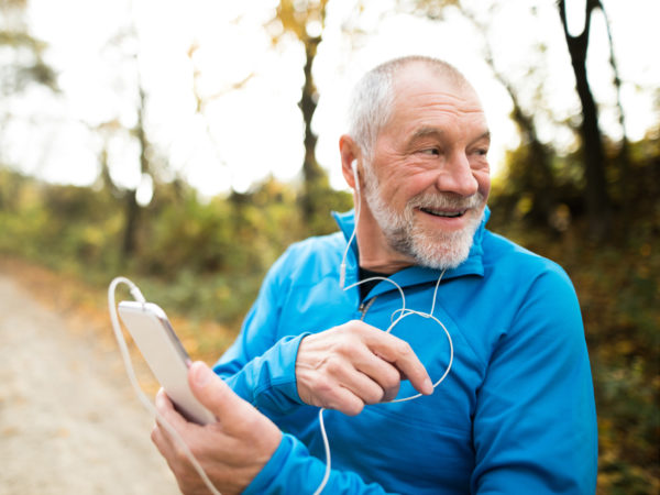 Senior runner in nature. Man with smart phone, listening to classical music.