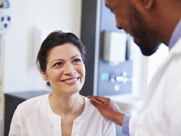 Female Patient Being Reassured By Doctor In Hospital Room