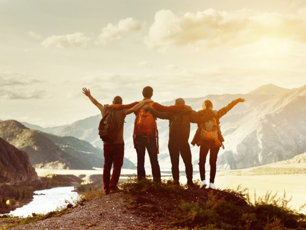 Four happy friends are looking on mountains and having fun together. Space for text. Travel concept