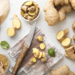 Raw fresh ginger root slices chopped with knife on wooden board with ginger powder on background.