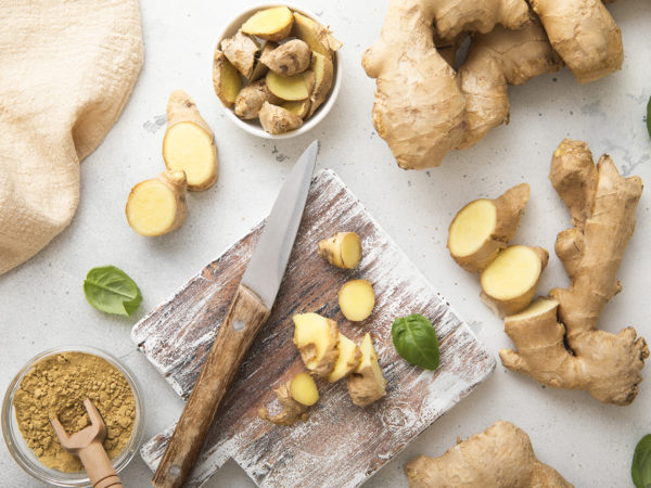 Raw fresh ginger root slices chopped with knife on wooden board with ginger powder on background.